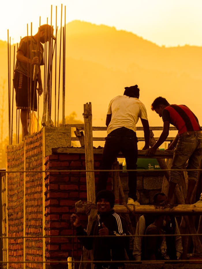 about-img A group of workers engaged in construction work on a brick structure during sunset.