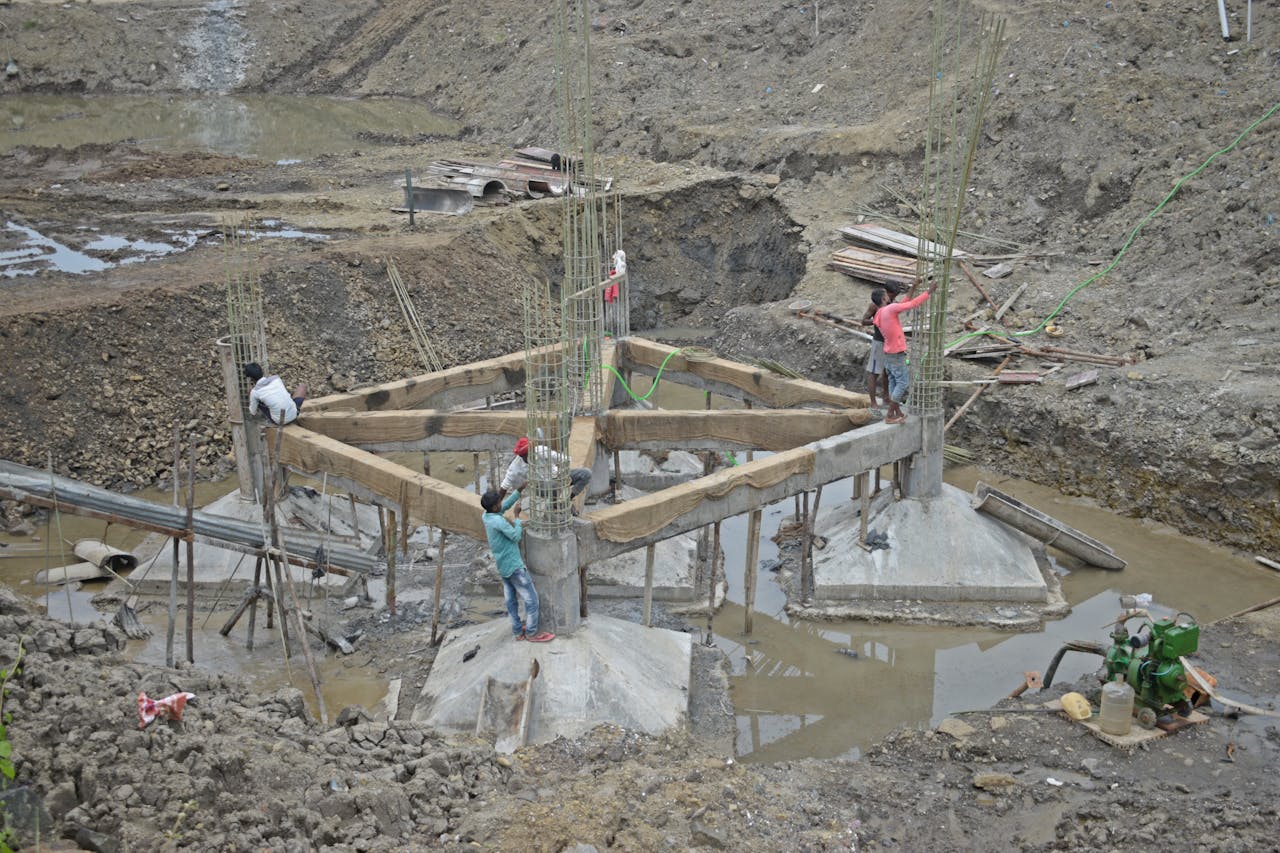 about-02 Workers constructing a building foundation with rebar and wooden supports outdoors.