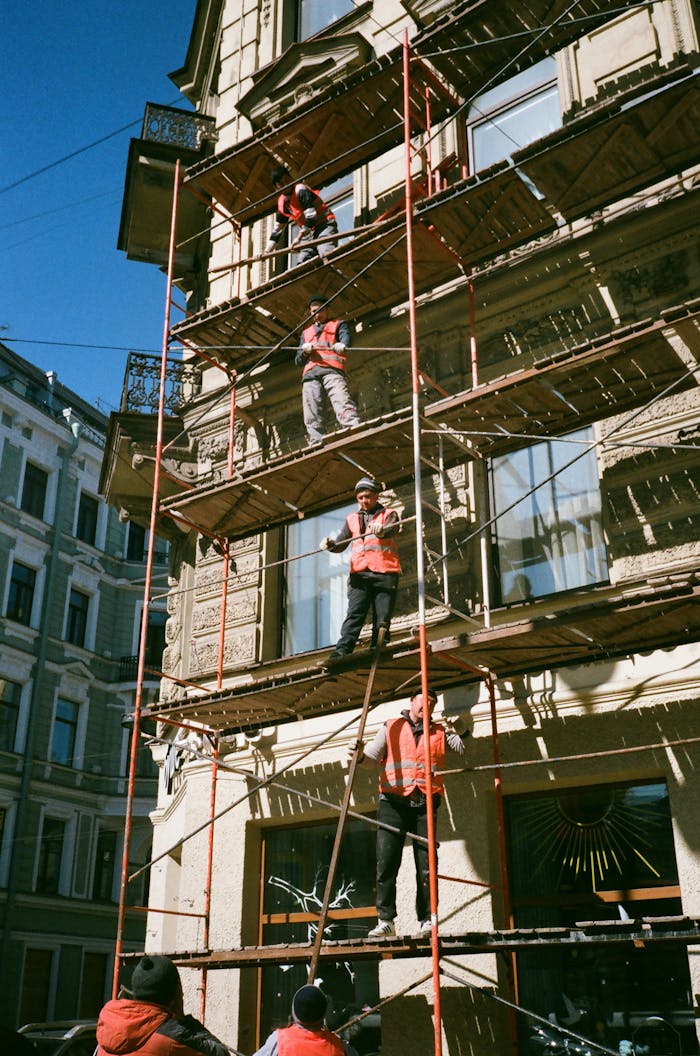 our-experience Construction workers on scaffolding renovating a building facade on a sunny day.