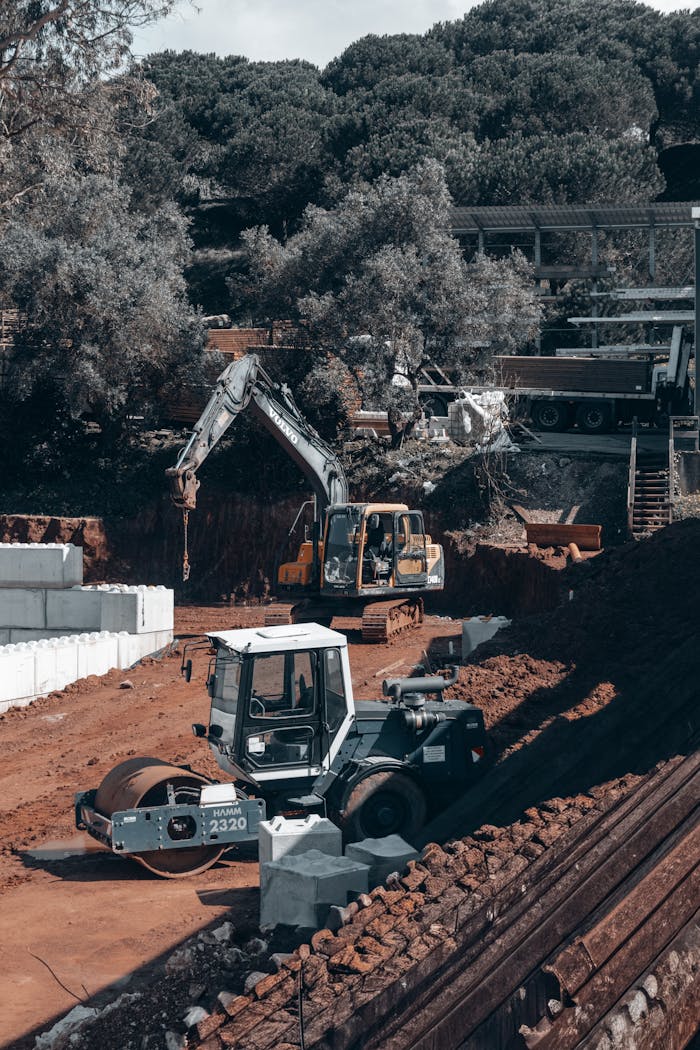 services-img Excavators and vehicles operate on a forested construction site under a clear sky.