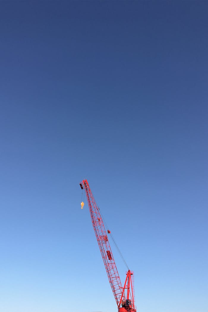 services-02 Red construction crane reaching into a clear blue sky, emphasizing industrial strength and potential.